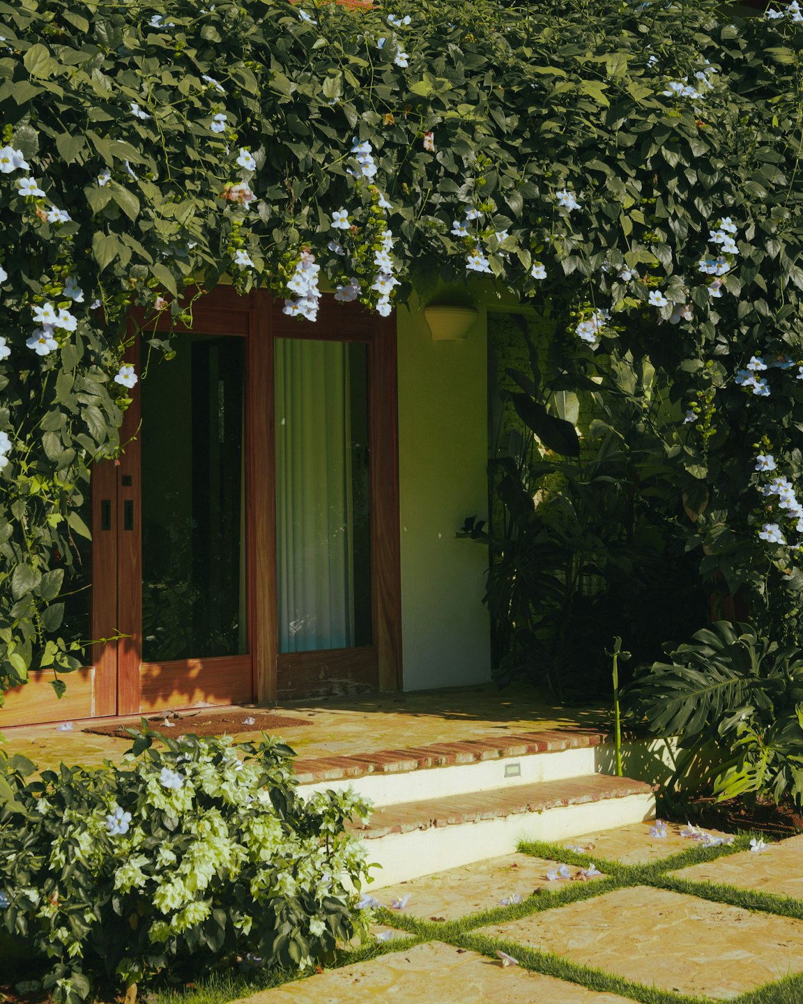 Une liane fleurie grimpe sur l'entrée à double porte en bois.